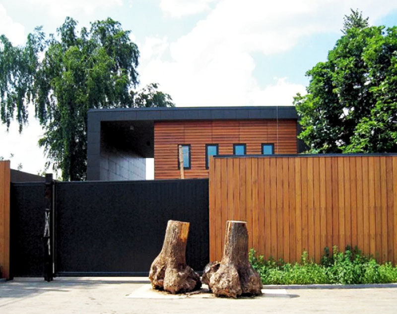 La casa está vallada por todos lados con una valla alta de madera, el área de entrada está decorada con un par de árboles arrancados y cultivados.