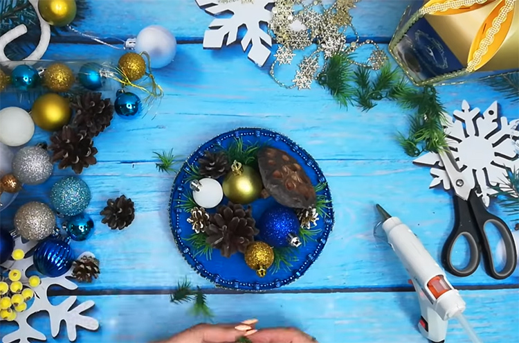 Decorate la base con addobbi per l'albero di Natale. Usa coni e palline, pezzi di rami di abete e altri materiali naturali