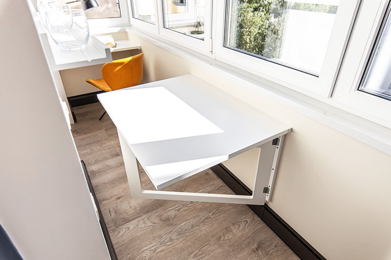 Bestel bij het organiseren van een kantoor op het balkon een klaptafel in de werkplaats - zodat u zich vrij kunt bewegen in een beperkte ruimte, gewoon door het deksel te laten zakken