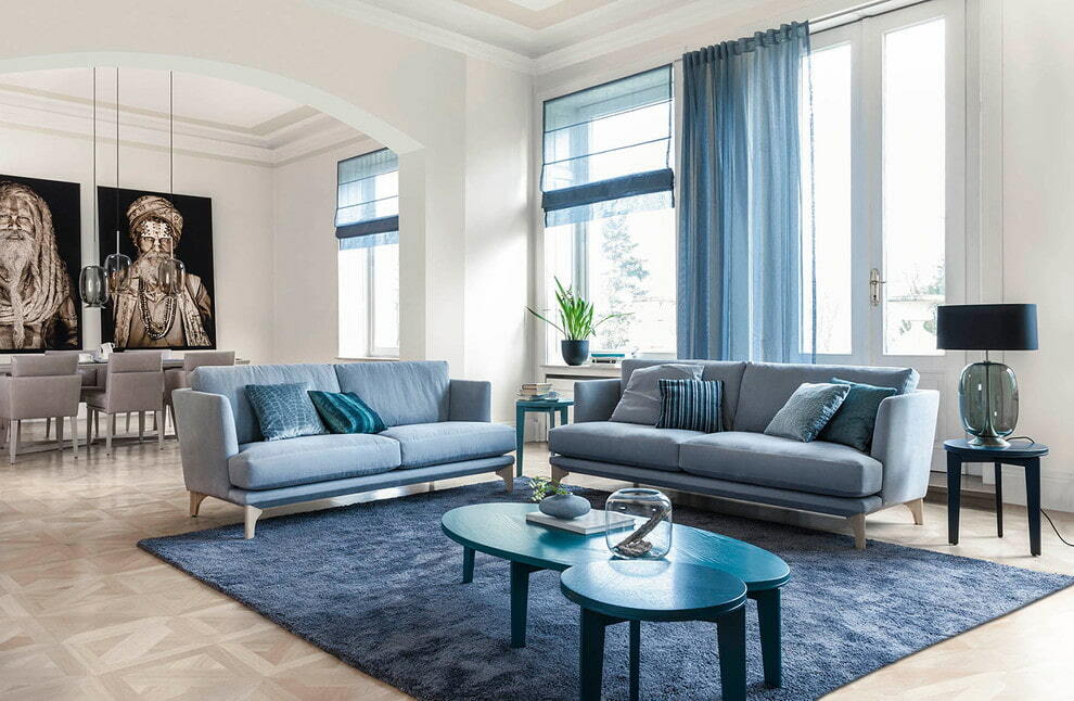 Dvě modré pohovky v obývacím pokoji s velkými okny