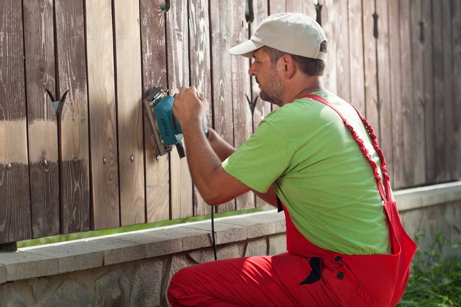 Grinding a wooden picket fence on a fence