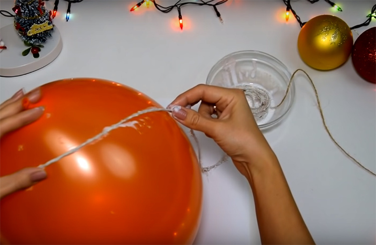 Remoja un hilo en pegamento diluido con agua y enrolla una bola inflada. No cortar el hilo, trabajar con toda la madeja hasta terminar