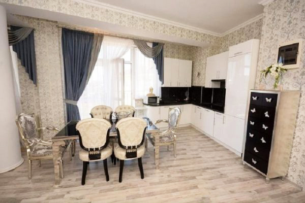 The kitchen area has a white glossy set and a set of furniture - a table and chairs