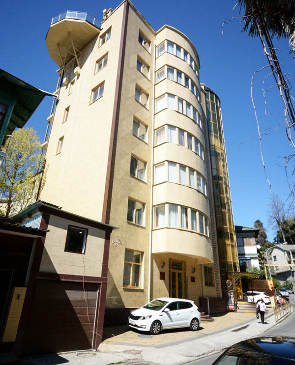 El edificio del hotel está pintado de blanco y se eleva junto a otras casas a lo largo de la calle.