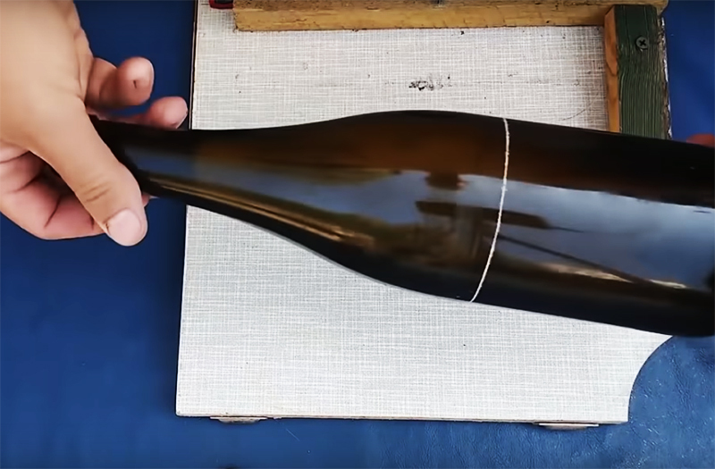 Wystarczy przymocować butelkę do deski tak, aby spód spoczywał na drewnianym narożniku i obracając ją wzdłuż osi, narysować prostą linię nożem do szkła