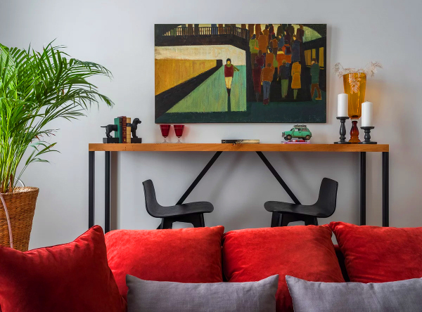 Das Wohnzimmer ist mit mehreren Gegenständen gleichzeitig dekoriert: einem Bild über dem Tisch, einer leuchtend gelb-orangenen Vase und einer großen Pflanze in einer Wanne