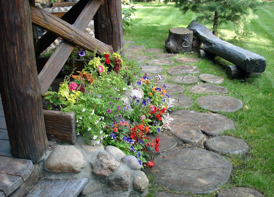 Gėlių lova kaimo stiliumi prie medinio pastato sienos