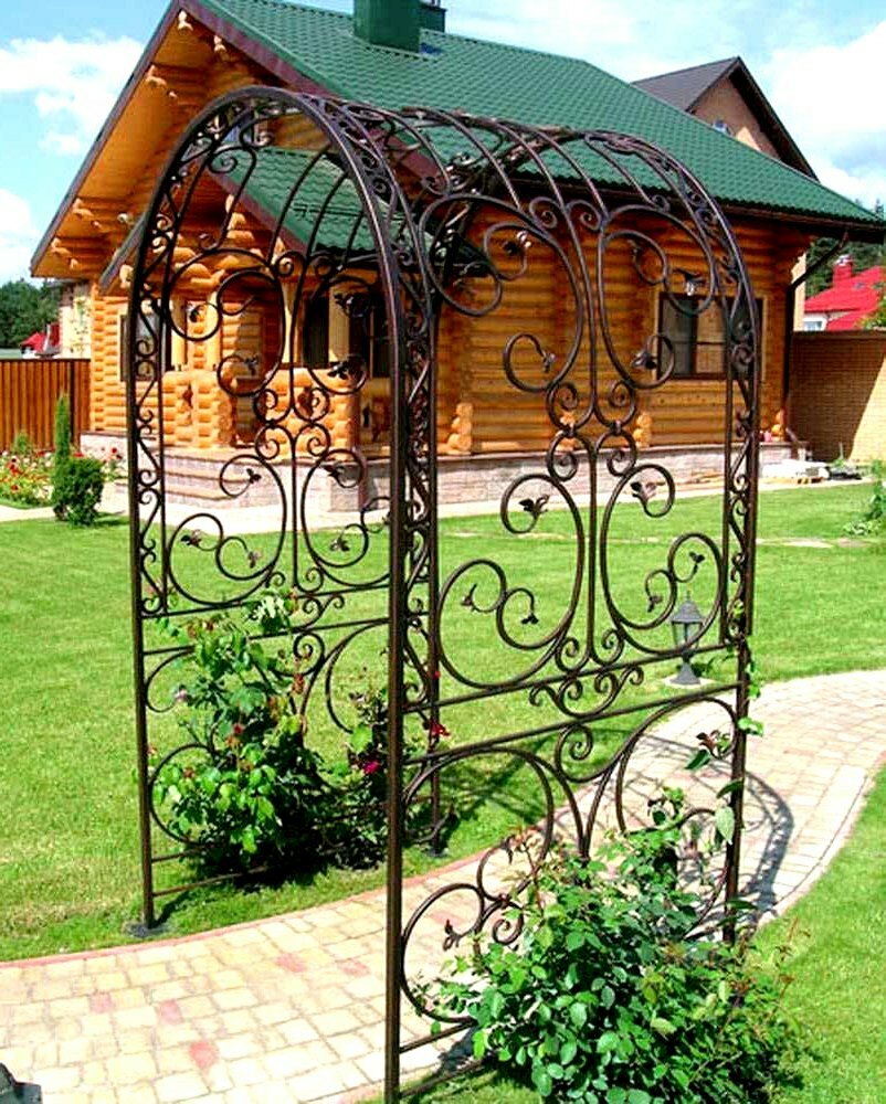 Openwork arch made of carbon steel on the site with a wooden house