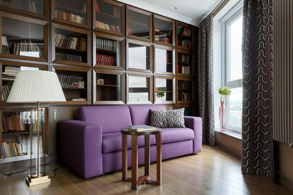 Violets dīvāns viesistabā ar mājas bibliotēku