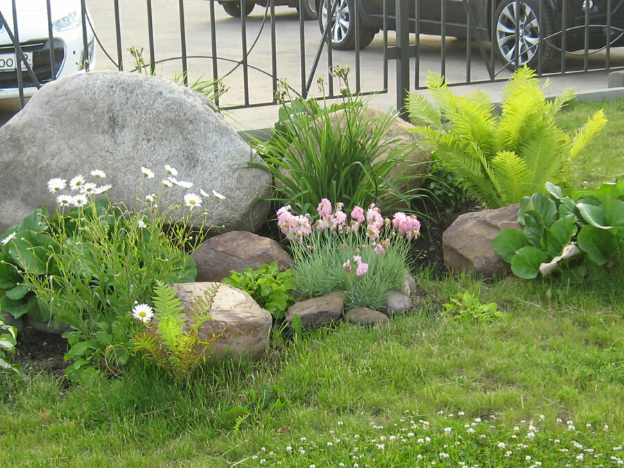 Grå steinblokk på et blomsterbed nær et metallgjerde