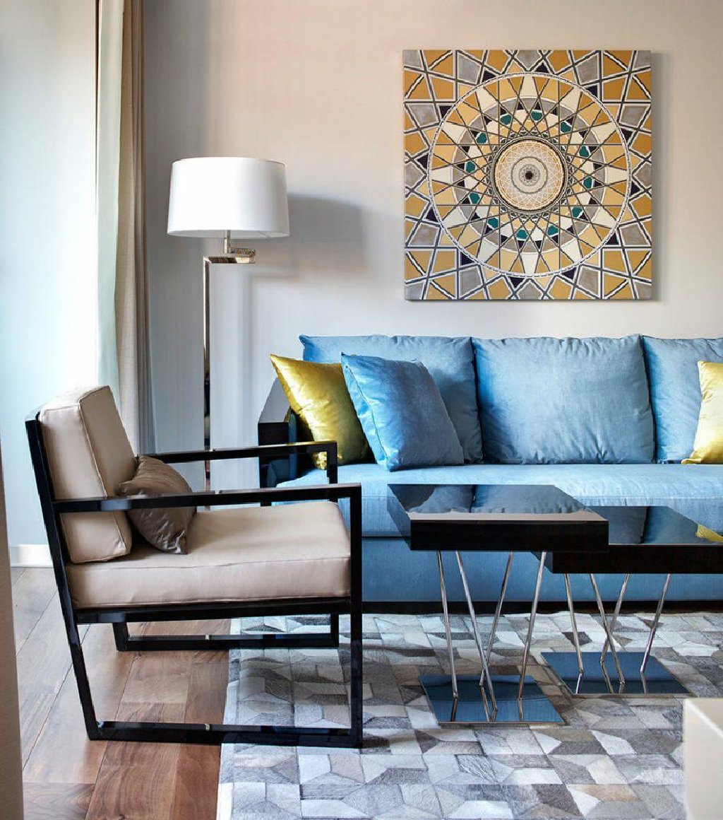 Négyzet alakú festmény egy kék kanapén egy lakásban