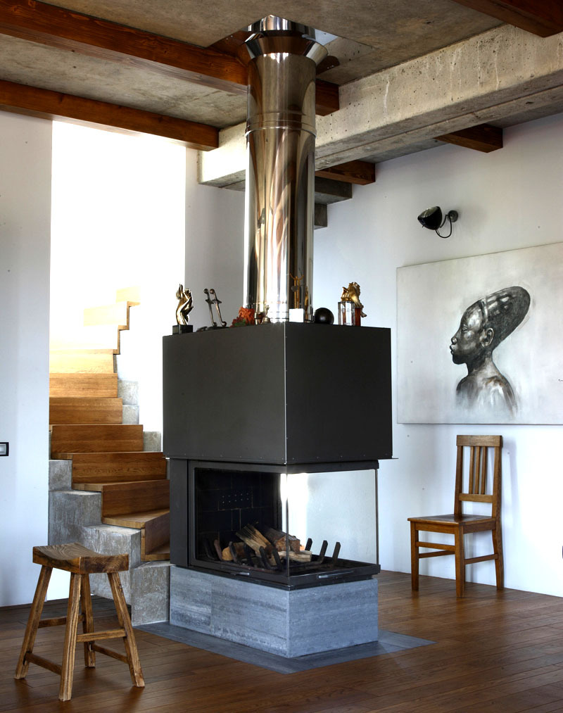A stylish fireplace with a chimney was installed near the stairs on a podium made of natural stone