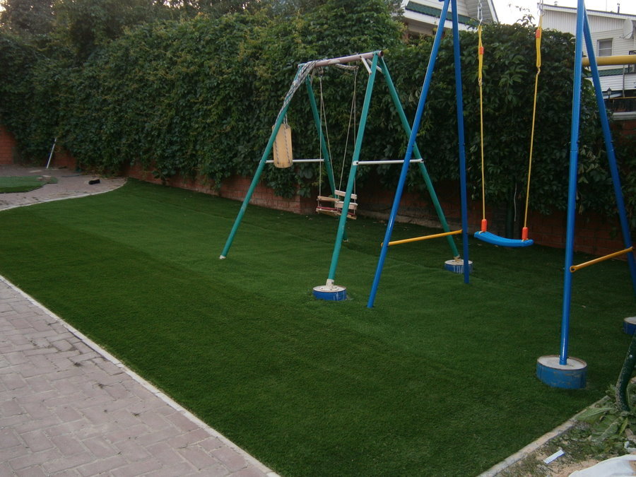 Huśtawka dziecięca na placu zabaw z trawnikiem sportowym