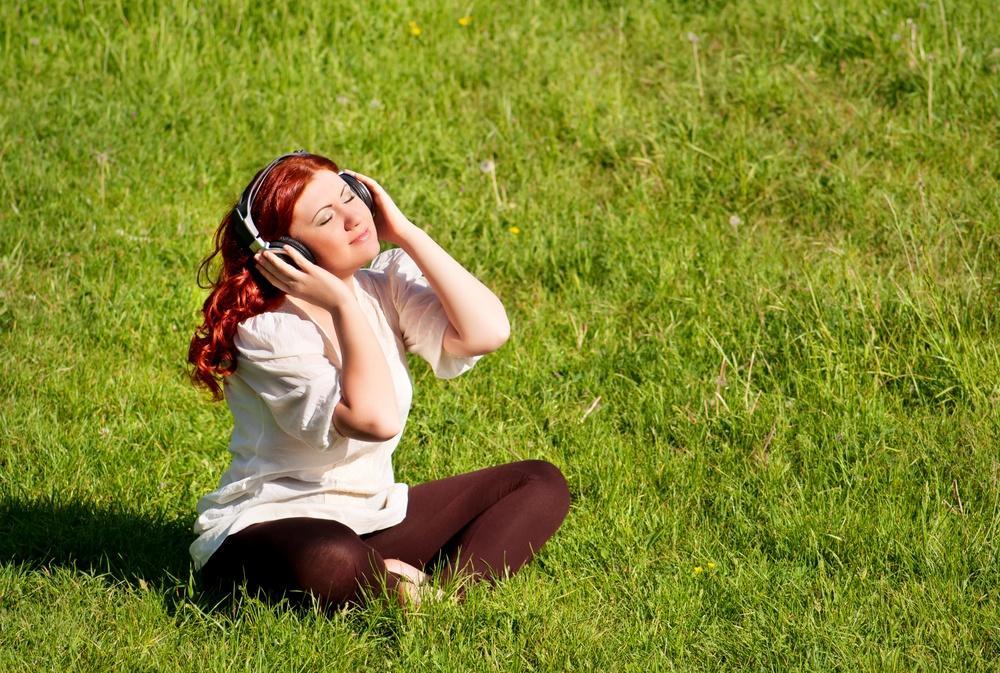 Mergina su ausinėmis ant pievos vejos