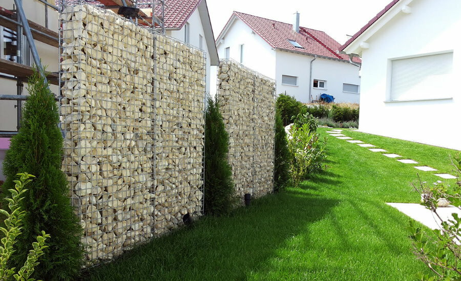 En vegg av smale gabioner mellom sommerhytter