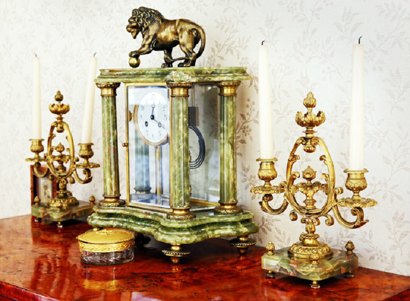 La parte superior de la cómoda está decorada con candelabros antiguos en dorado y un antiguo reloj mecánico de cuerda manual.